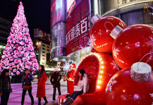 In Cina sono usuali i grandi addobbi nei pressi dei centri commerciali. Qui, una ragazza cinese posa per una foto seduta su una poltrona a forma di palla natalizia